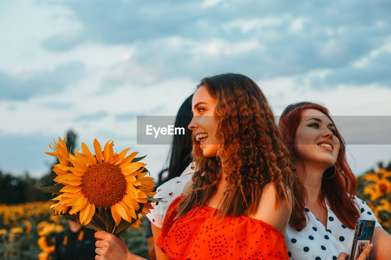 BEAUTIFUL YOUNG WOMAN WITH FLOWER AGAINST SKY