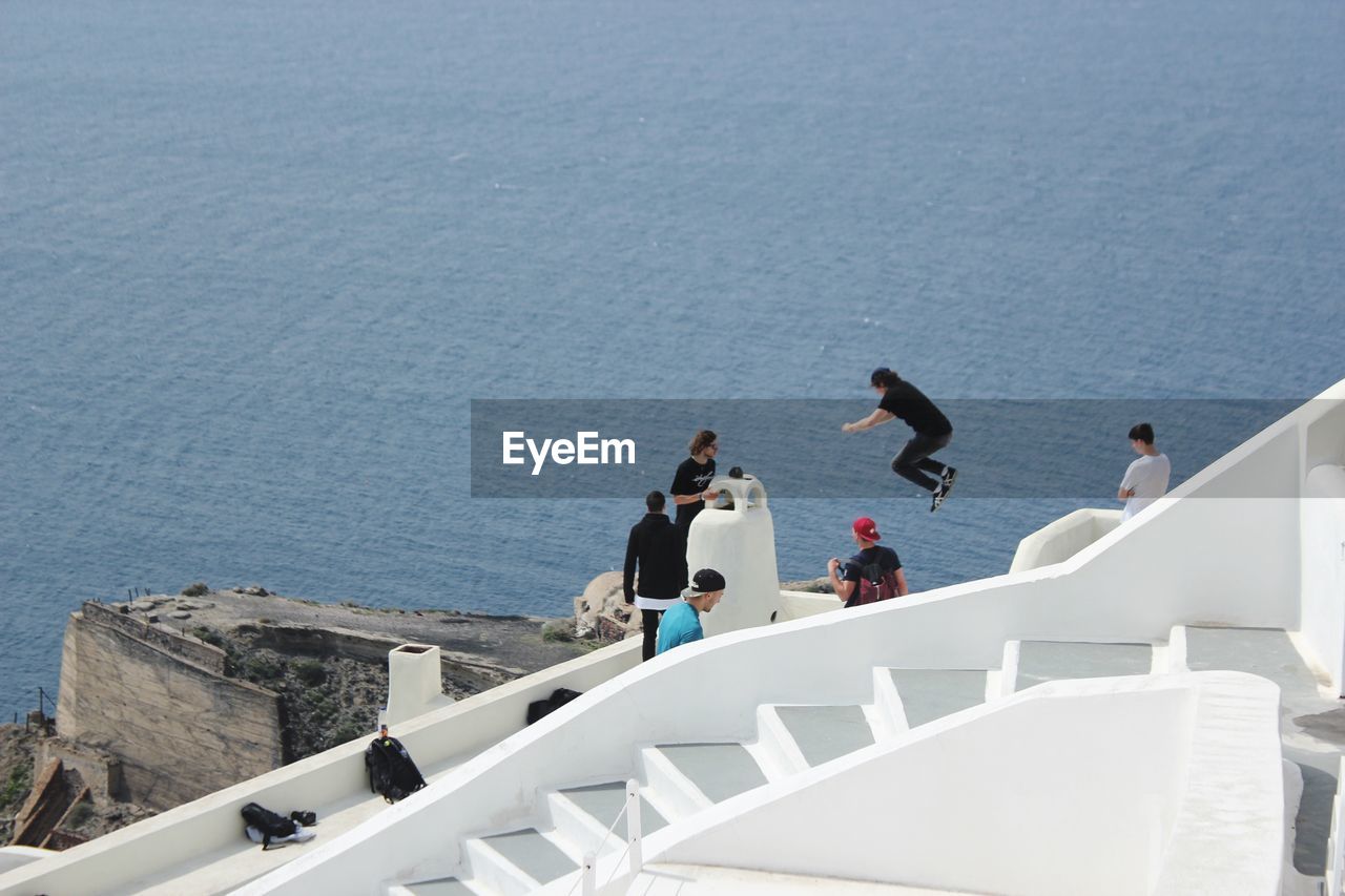 HIGH ANGLE VIEW OF PEOPLE JUMPING OVER SEA AGAINST BUILDINGS