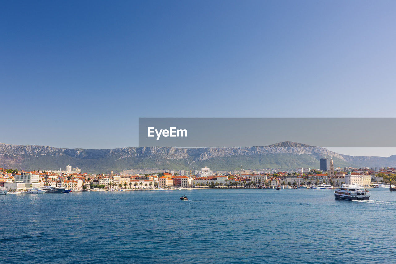 water, architecture, sky, sea, city, transportation, building exterior, clear sky, nautical vessel, ship, vehicle, nature, built structure, mountain, travel destinations, horizon, building, blue, mode of transportation, travel, coast, no people, harbor, bay, waterfront, copy space, cityscape, body of water, land, day, scenics - nature, outdoors, boat, beauty in nature, marina, shore, vacation, ocean, tourism, sunny, town, passenger ship, beach, residential district, landscape, dusk