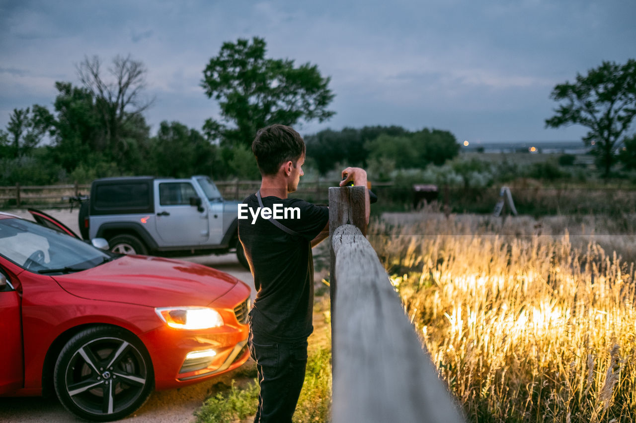 MAN STANDING BY CAR ON FIELD