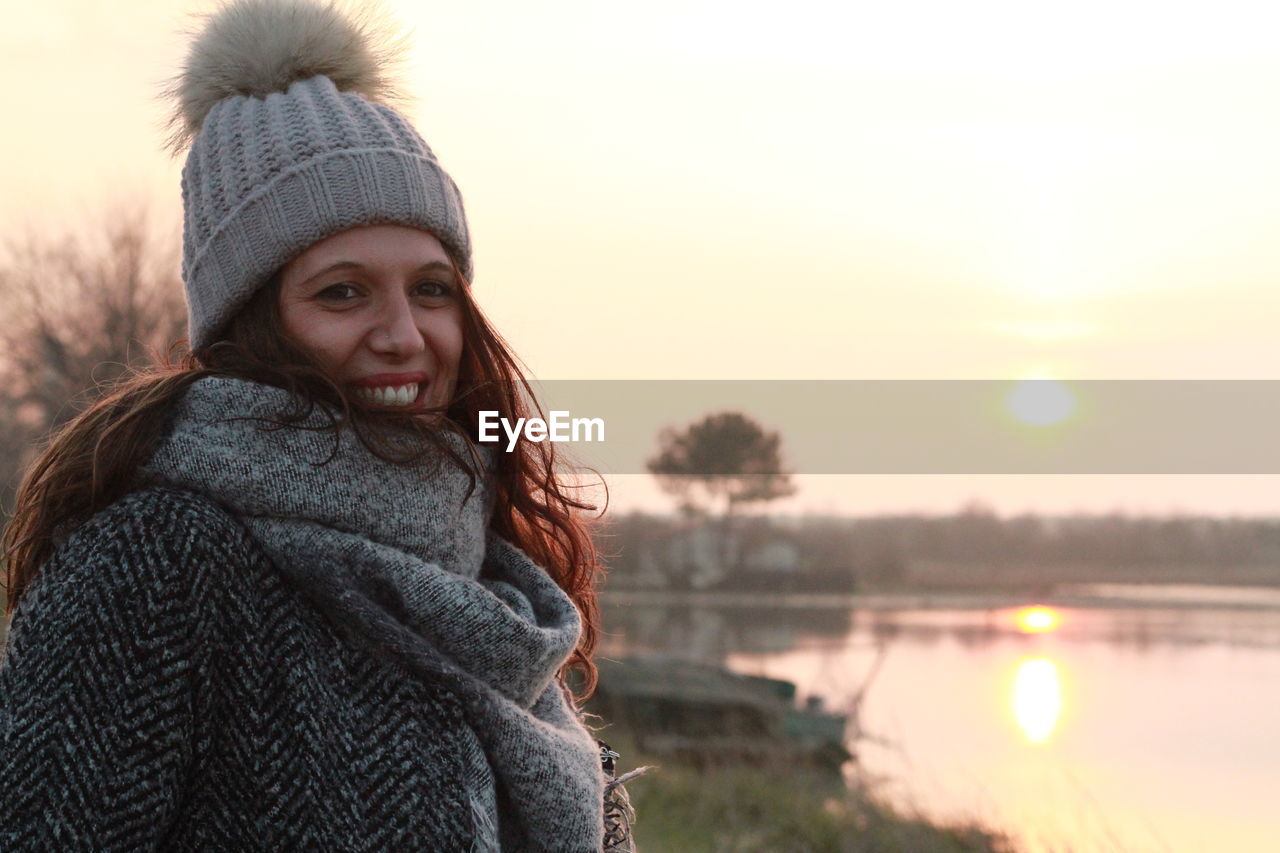 Portrait of woman standing by river against sky during sunset