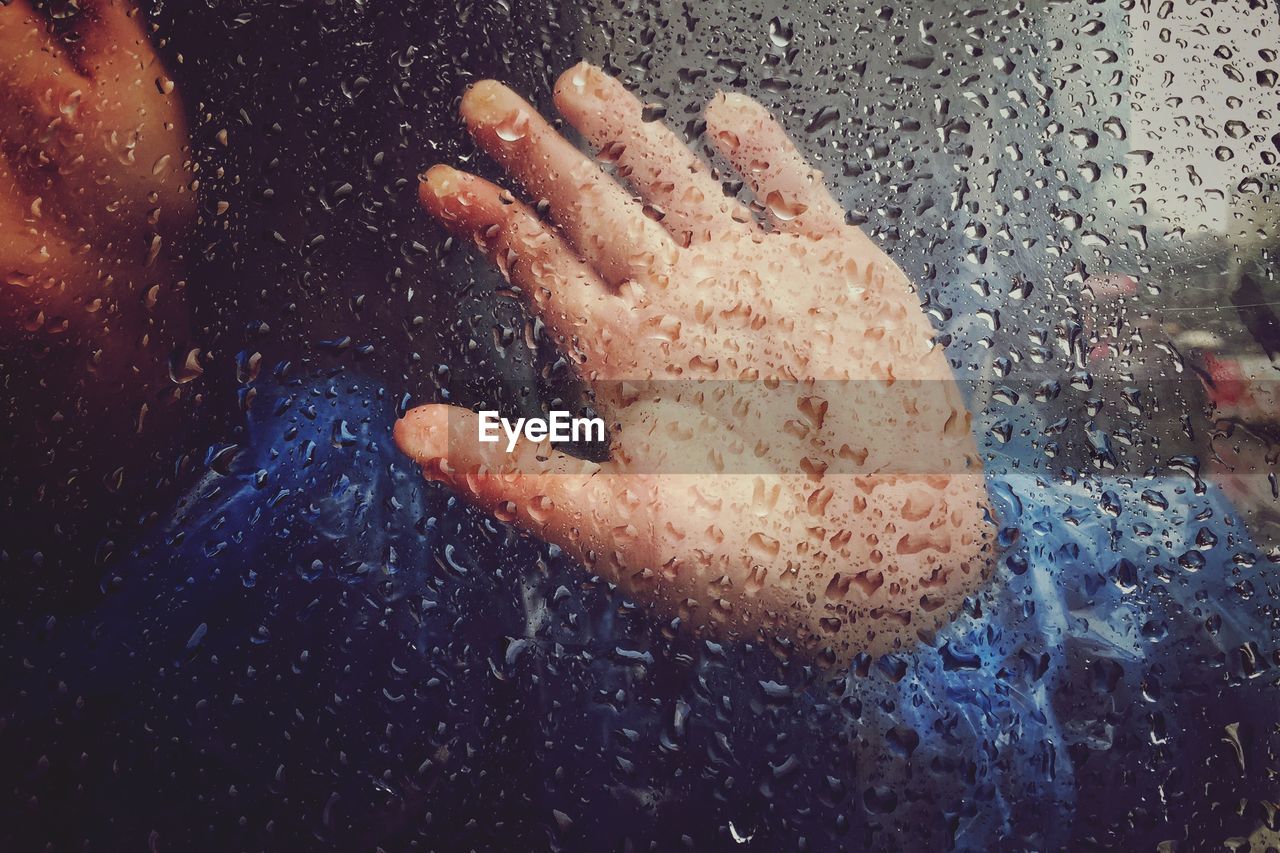 Cropped hand on wet glass during rainy season
