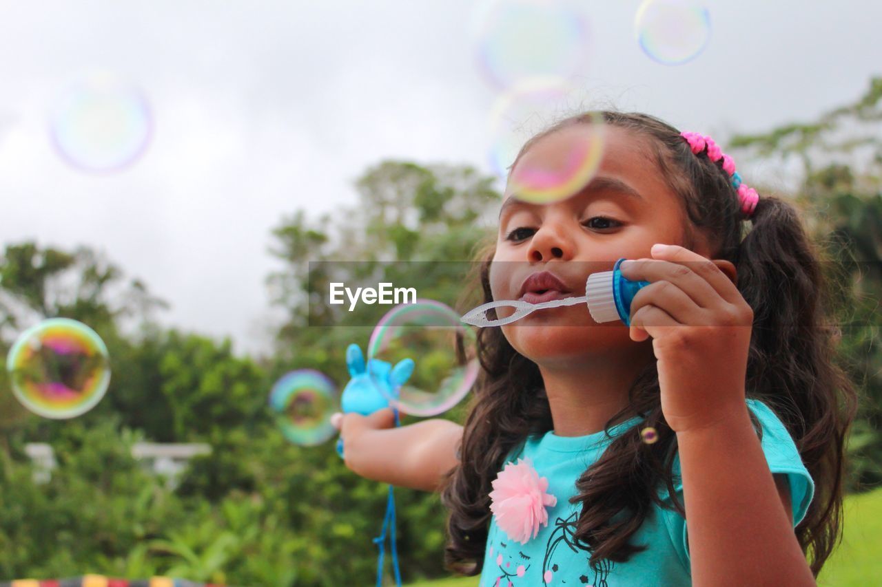 Girl blowing bubbles on field against trees