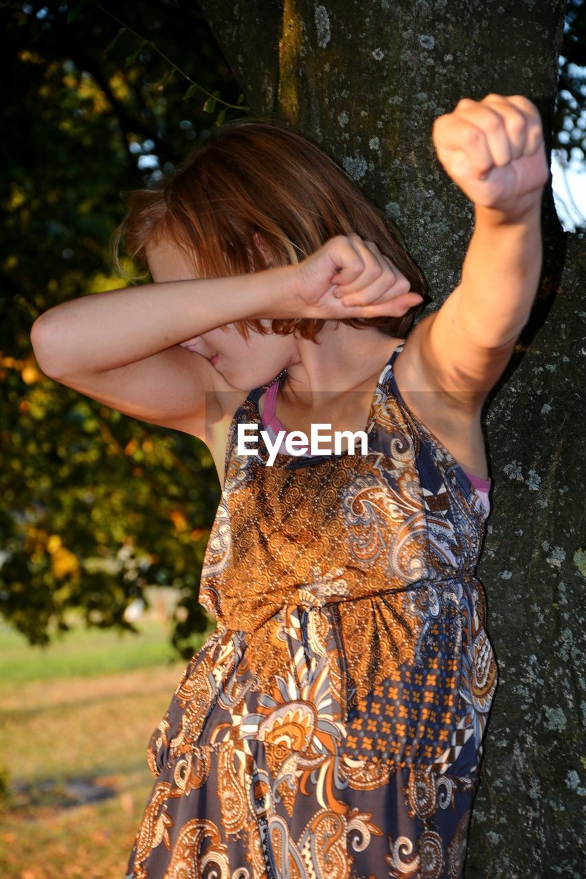 Girl covering face while standing against tree