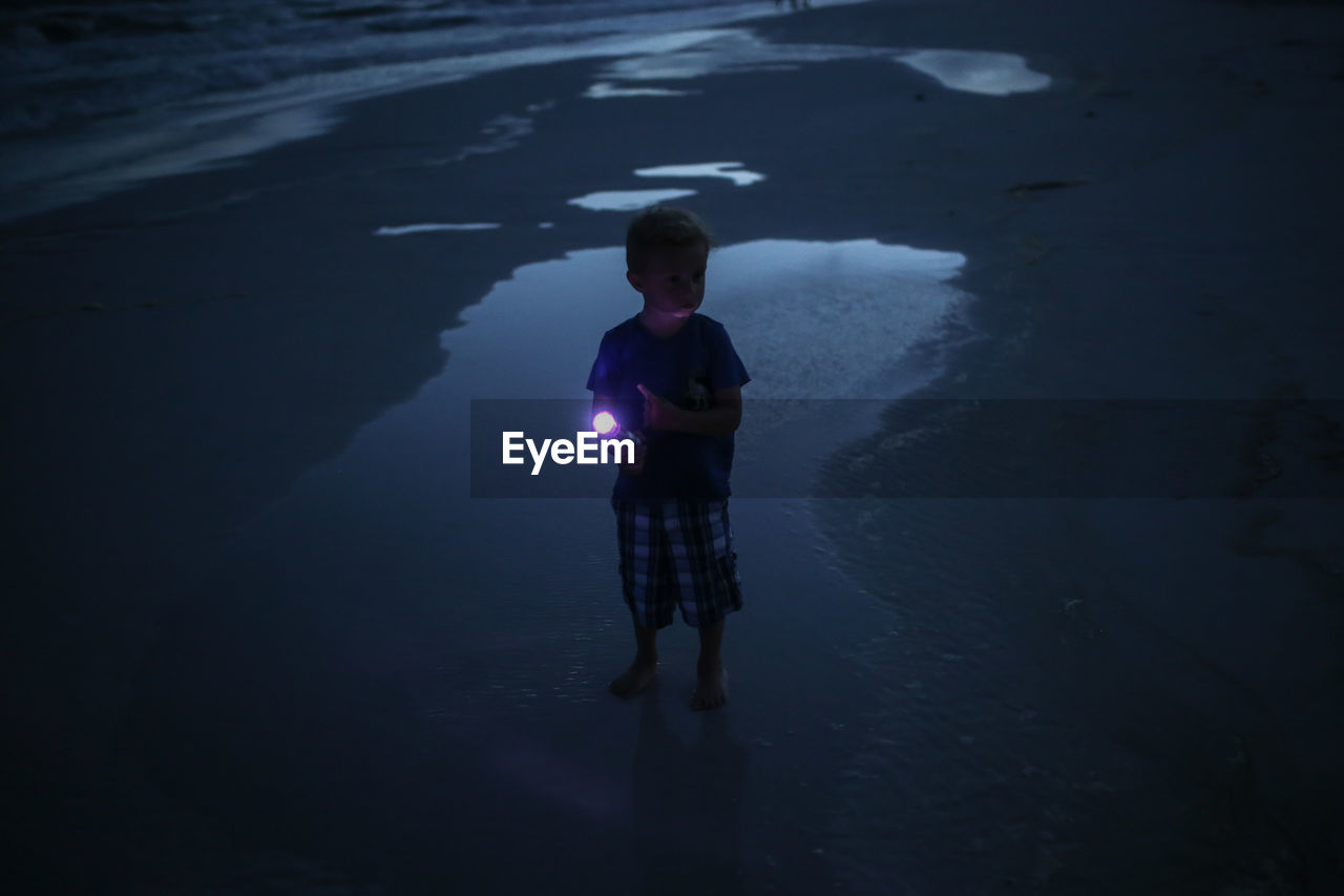 High angle view of boy holding flashlight while standing at beach