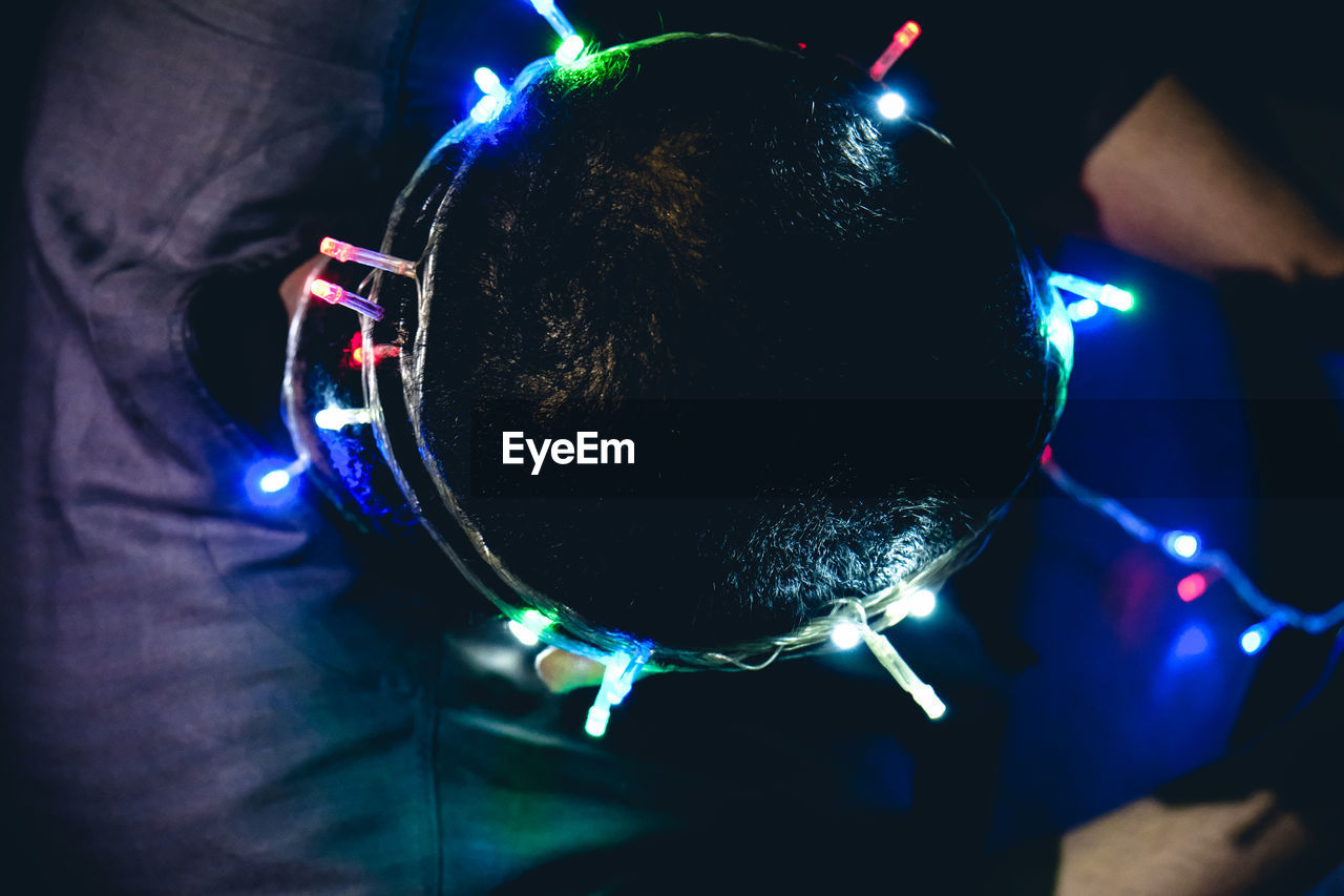 Directly above shot of man wearing illuminated christmas lights on head in darkroom