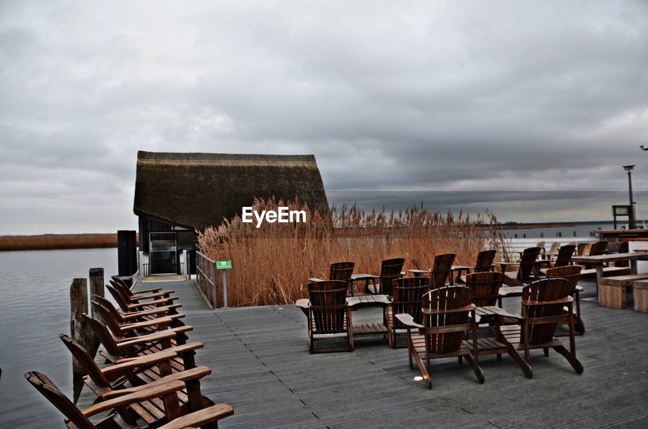 EMPTY CHAIRS AND TABLES IN ROW AGAINST SEA