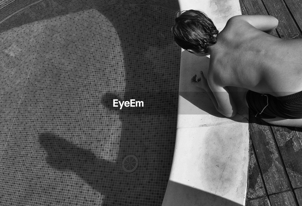 High angle view of shirtless boy kneeling on poolside