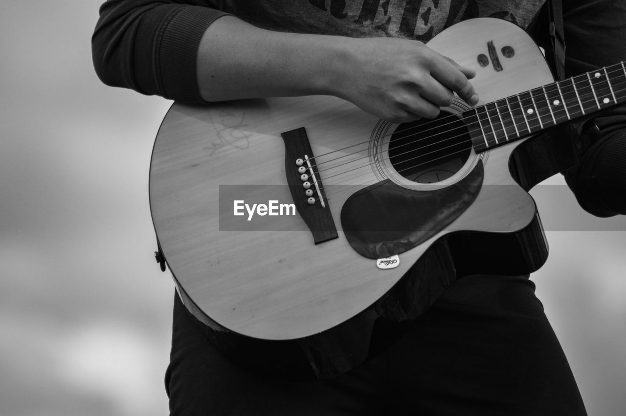 MIDSECTION OF MAN PLAYING GUITAR AT CAMERA