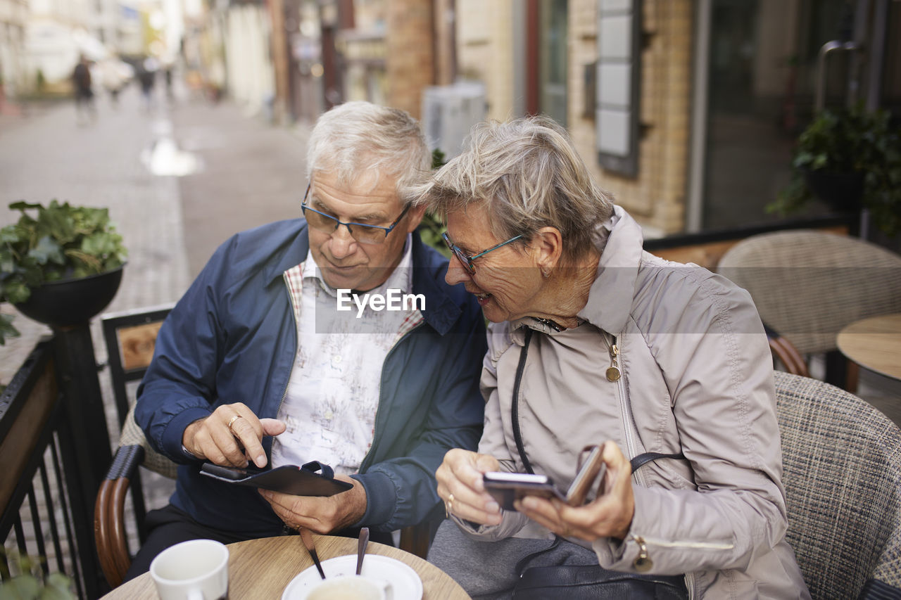 Mature couple in outdoor cafe using phones