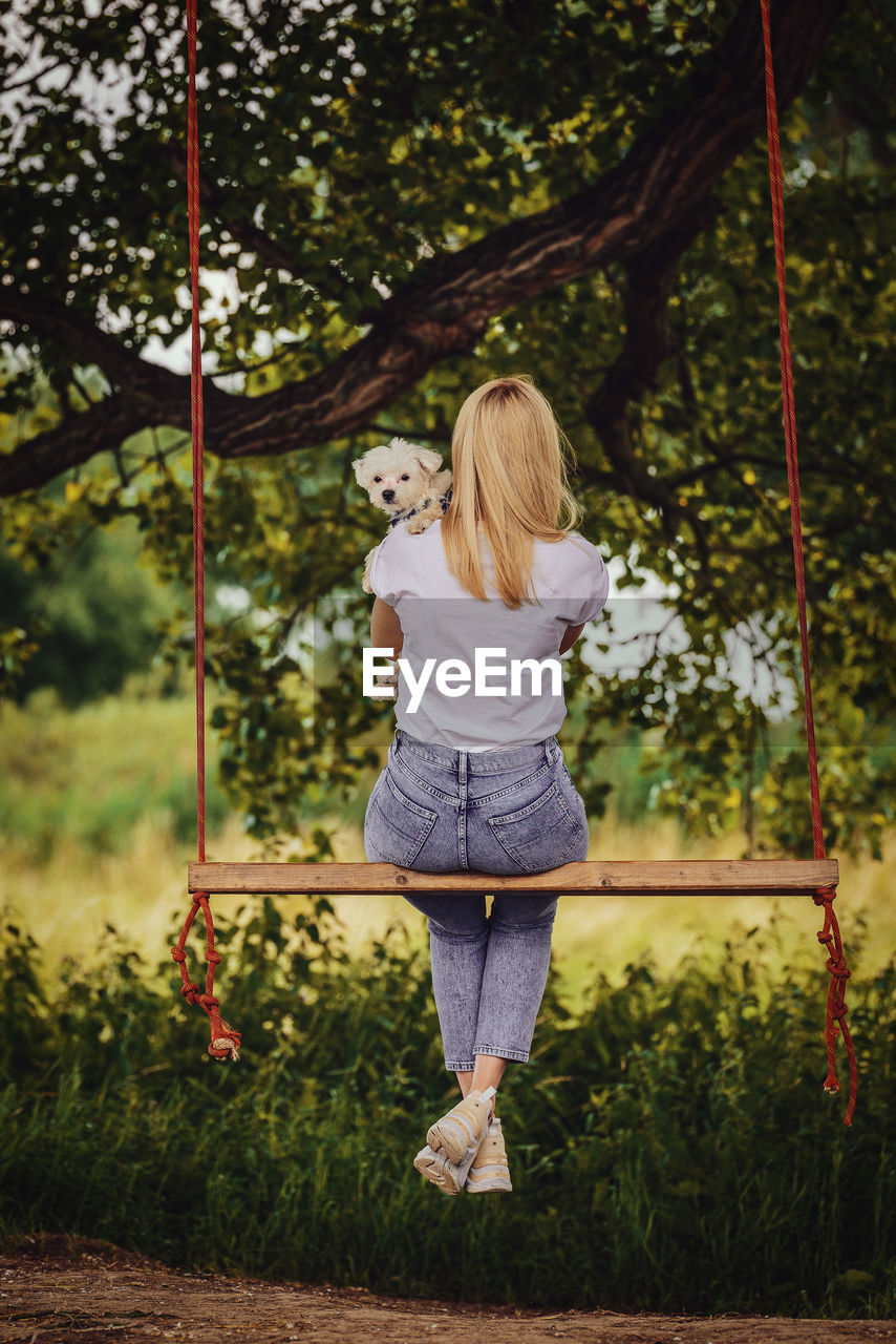 Young woman with a white dog on a tree swing.