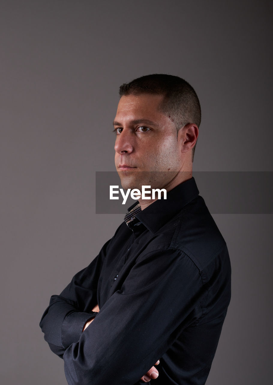 studio shot, one person, portrait, adult, indoors, men, gray background, arms crossed, gray, serious, looking at camera, formal wear, business, waist up, shaved head, black, standing, businessman, clothing, young adult, person, outerwear, business finance and industry, collar, mature adult, emotion, looking, copy space, tuxedo, side view