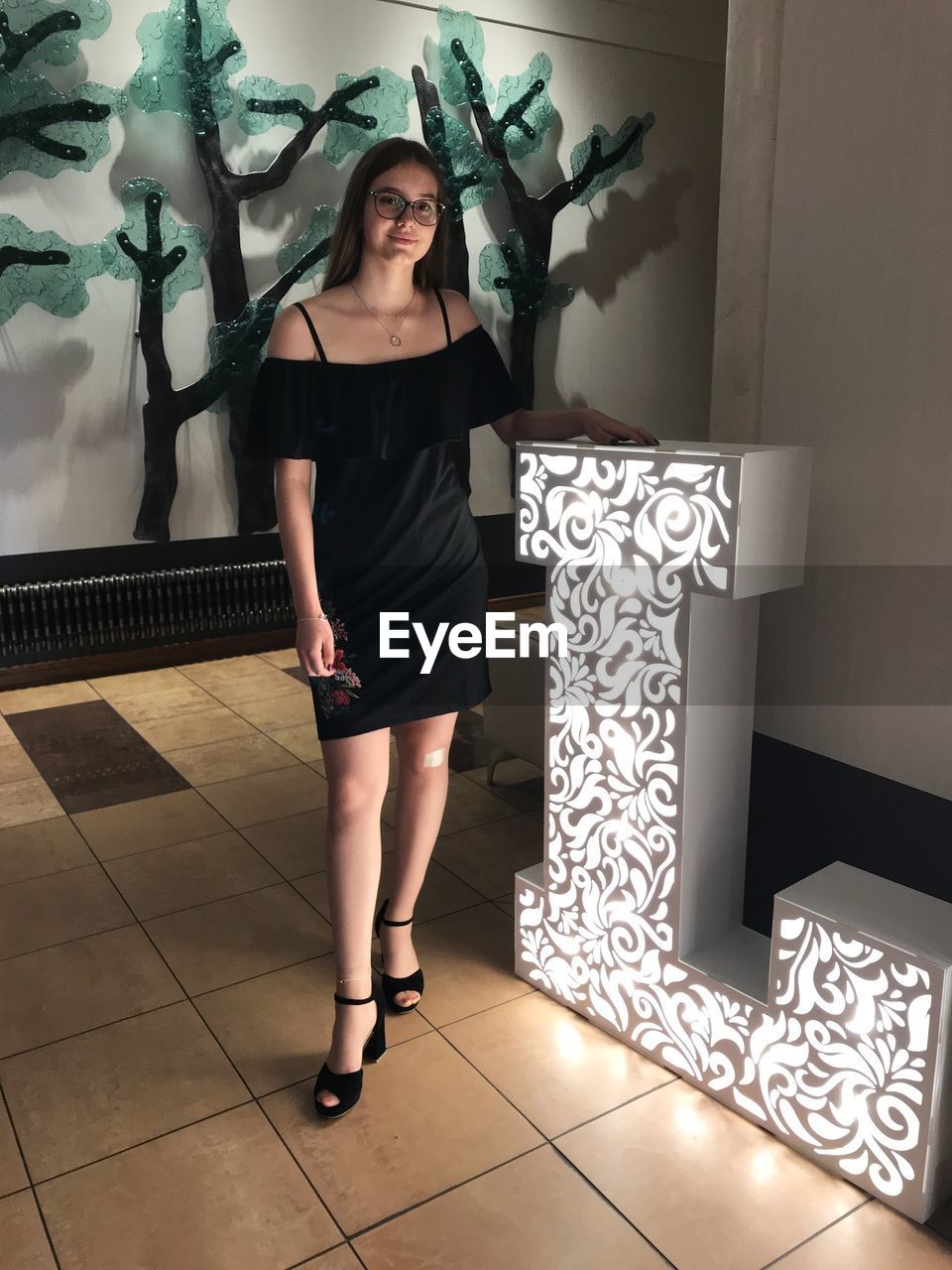 Portrait of teenage girl standing by illuminated alphabet l on tiled floor