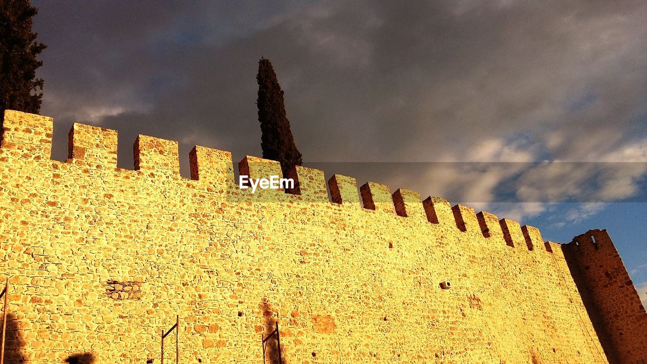 Low angle view of stone wall against cloudy sky