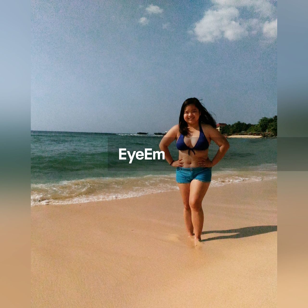 PORTRAIT OF YOUNG WOMAN ON BEACH AGAINST SKY