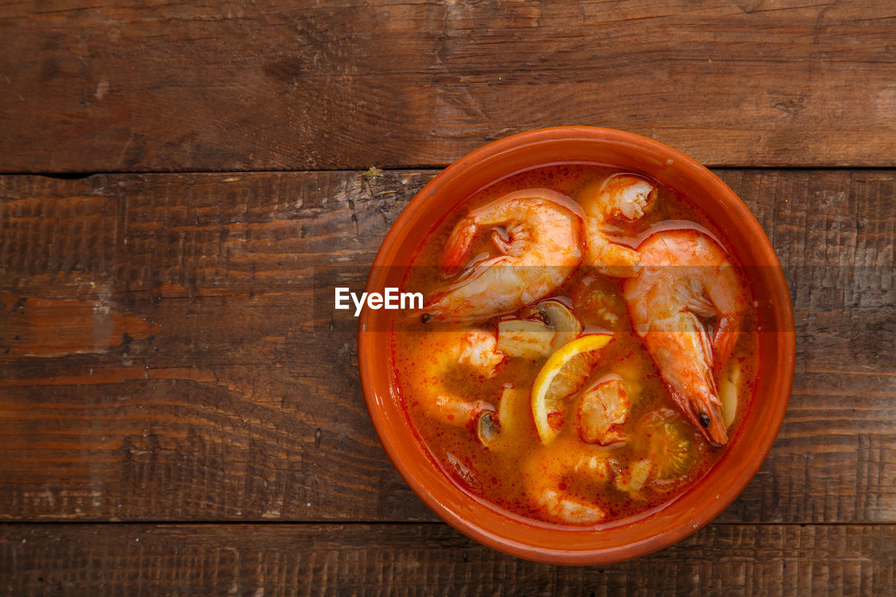 Tom yam soup with shrimps in a plate on a wooden table horizontal photo