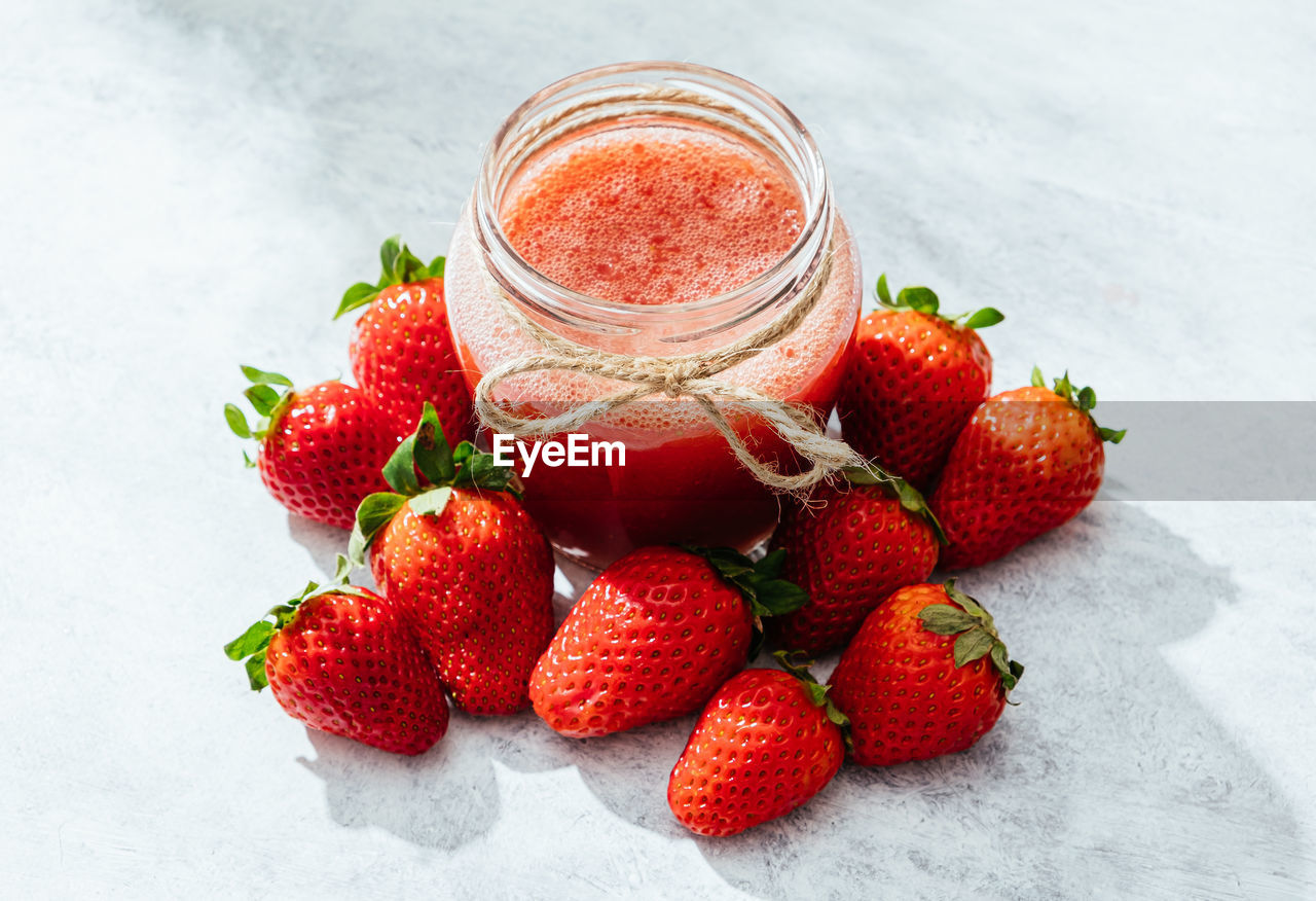 Composition with fresh homemade strawberry juice in glass jar wrapped with twine placed on marble surface with whole berries