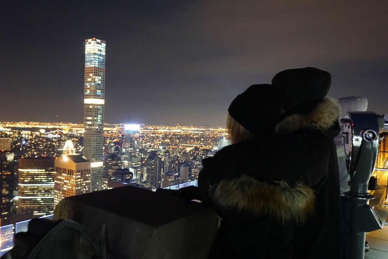 Side view of people looking at illuminated cityscape from observation point