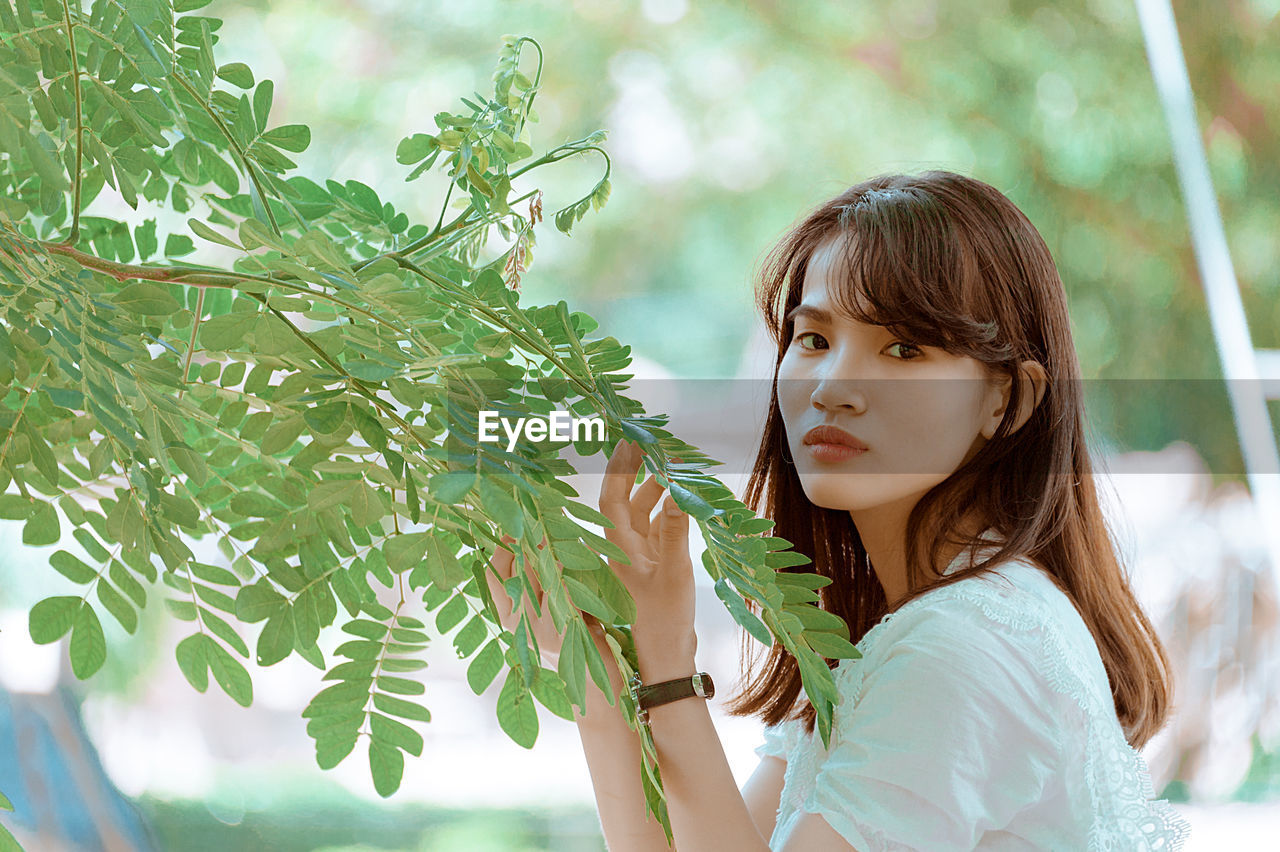 Side view portrait of young woman holding branches at park