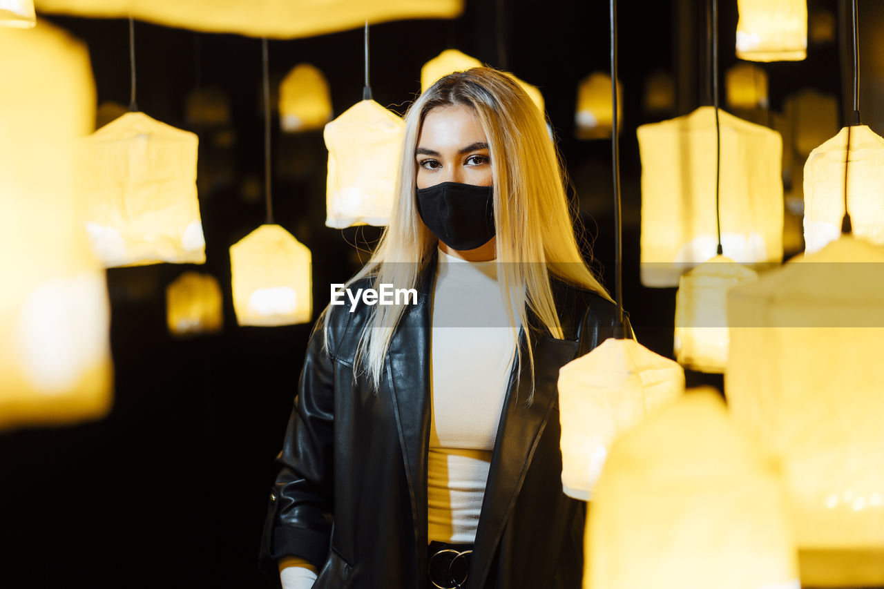 Young woman wearing protective face mask standing in between lamp