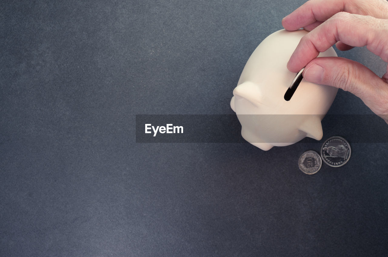 Close-up of hand putting coins in piggy bank over white background