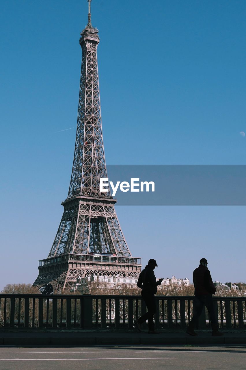 People walking by eiffel tower against clear blue sky