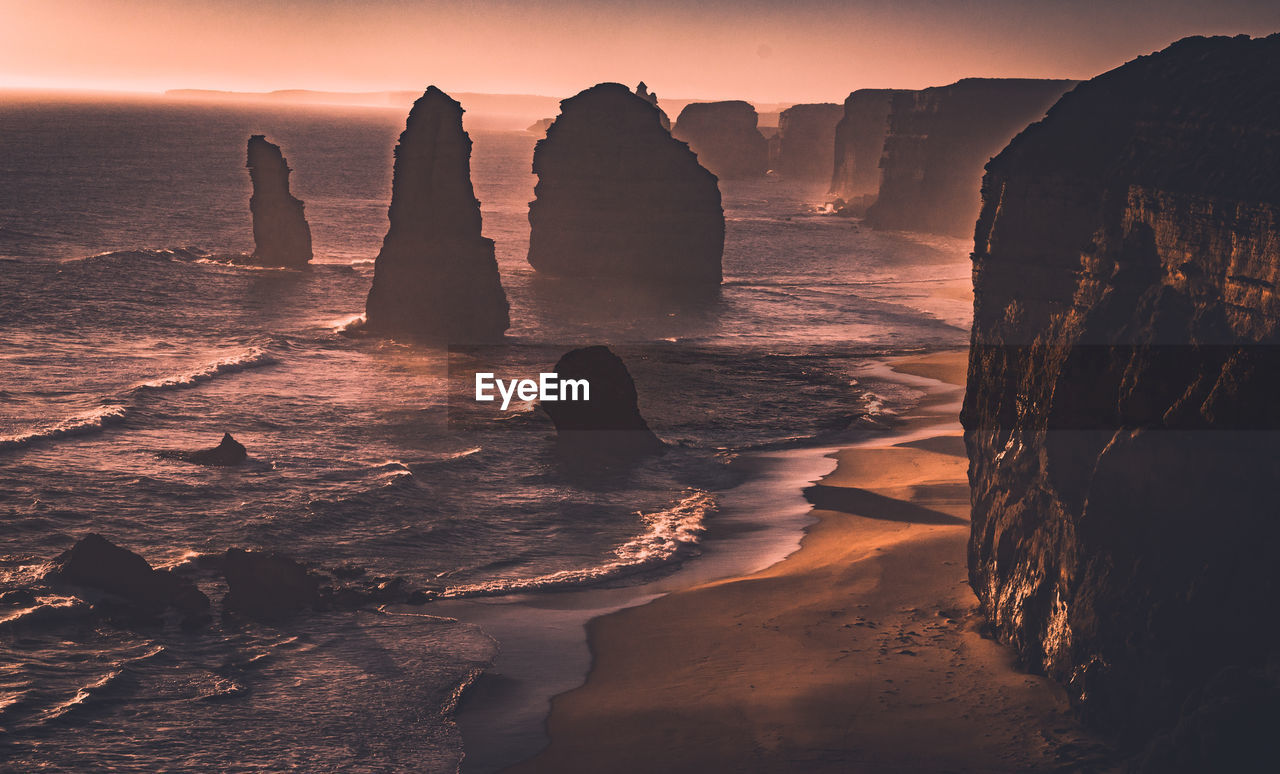 ROCK FORMATIONS AT SHORE AGAINST SKY DURING SUNSET