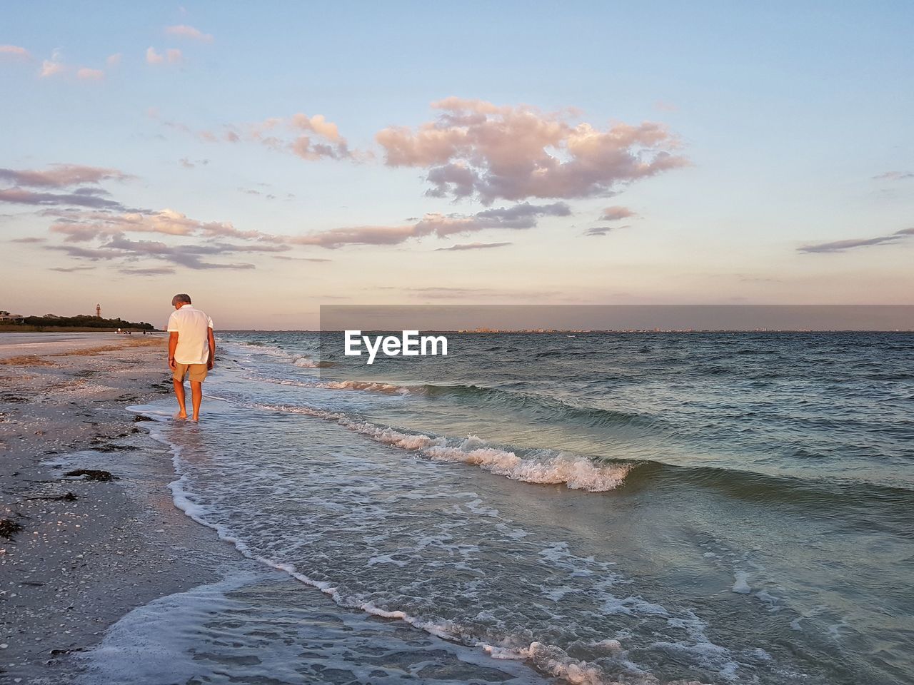 Rear view of man walking at beach against sky during sunset