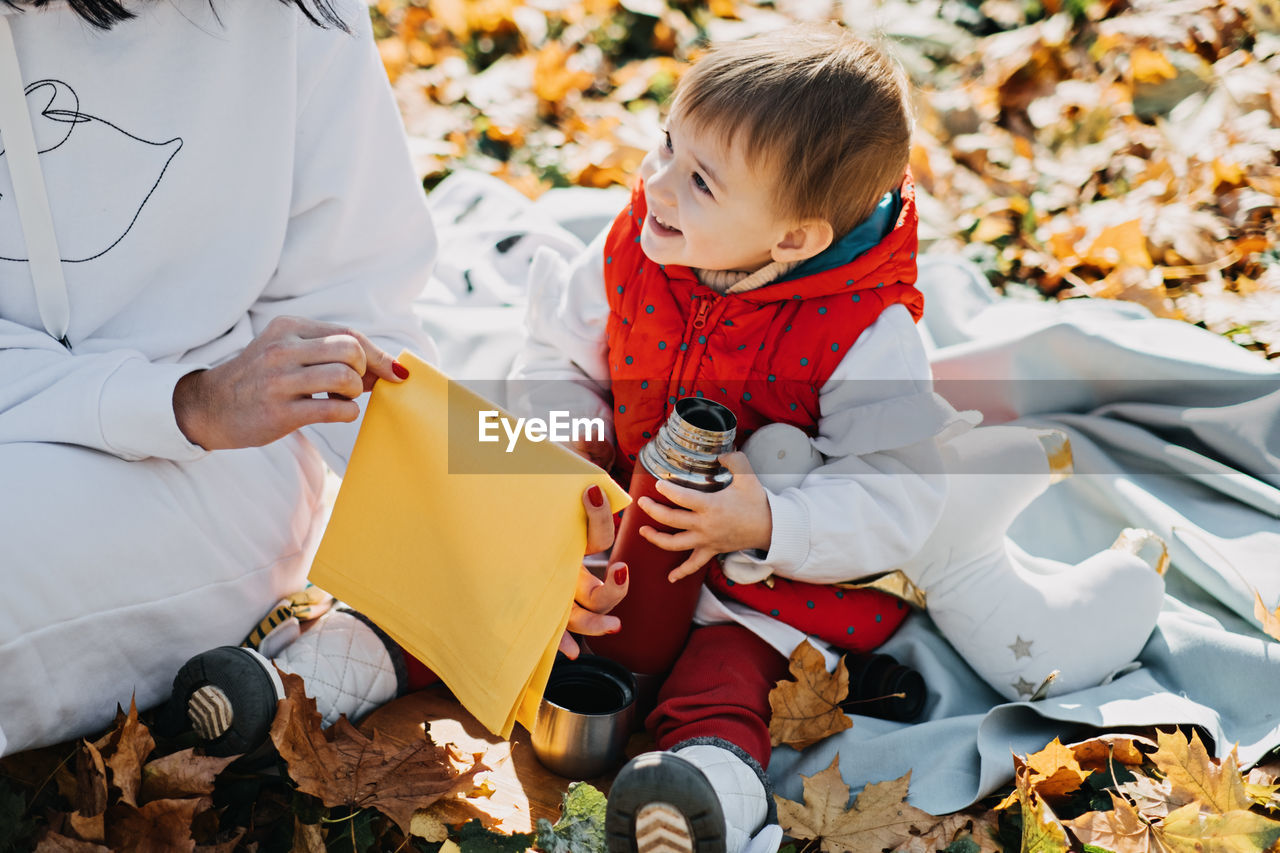 Happy family mother and little toddler baby daughter having autumn picnic with red thermos and cup