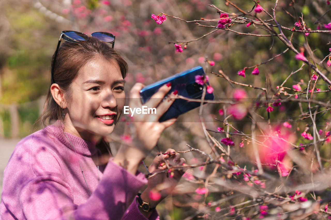 Smiling woman photographing pink flowers with mobile phone