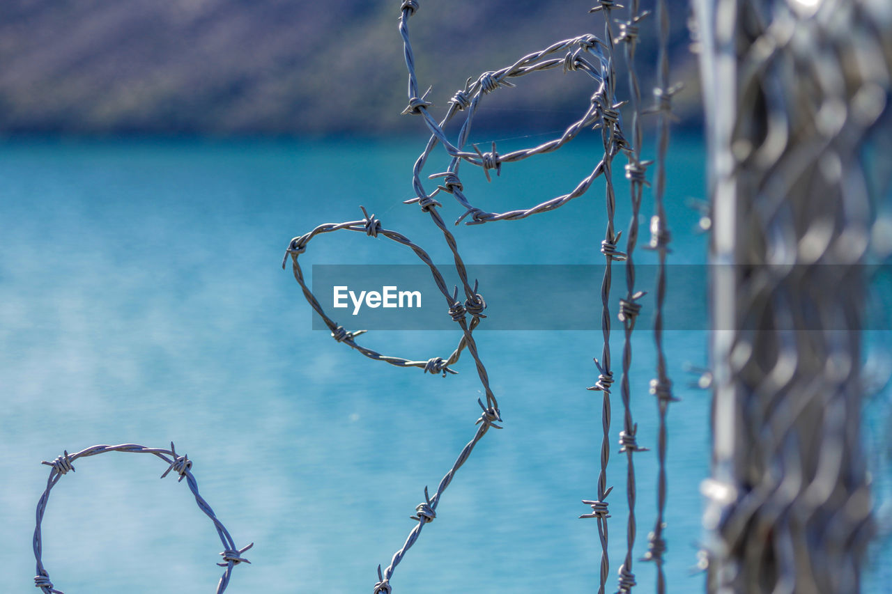 CLOSE-UP OF BARBED WIRE FENCE AGAINST BLUE WATER