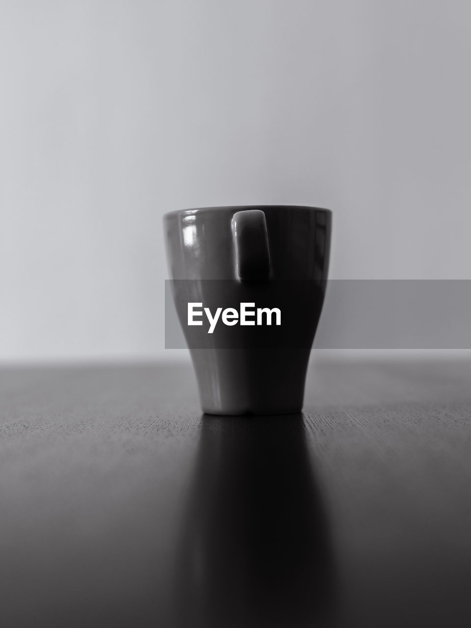 CLOSE-UP OF EMPTY COFFEE CUP ON TABLE WITH GLASS