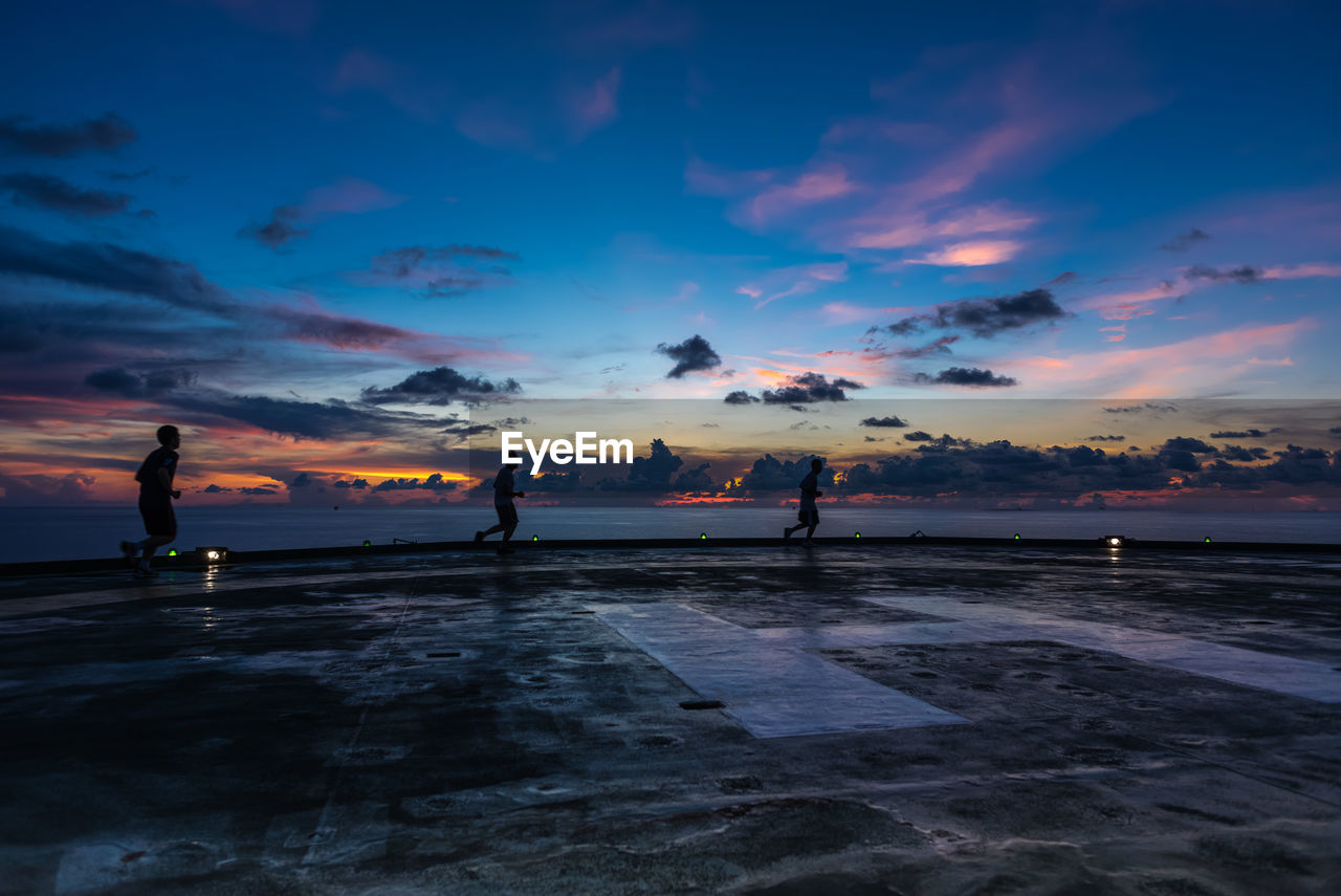 Silhouette people at beach against sky during sunset