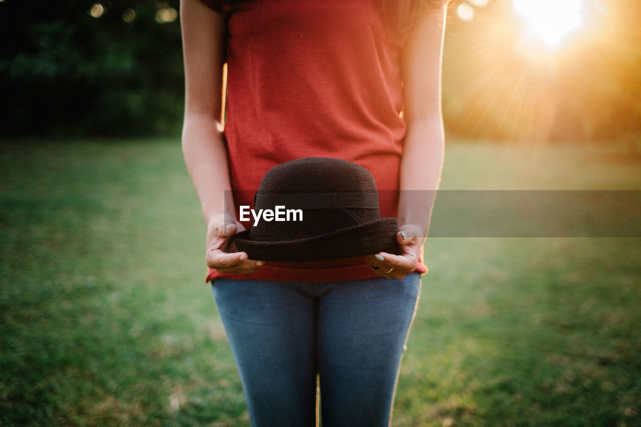 Midsection of woman holding black hat on field during sunny day