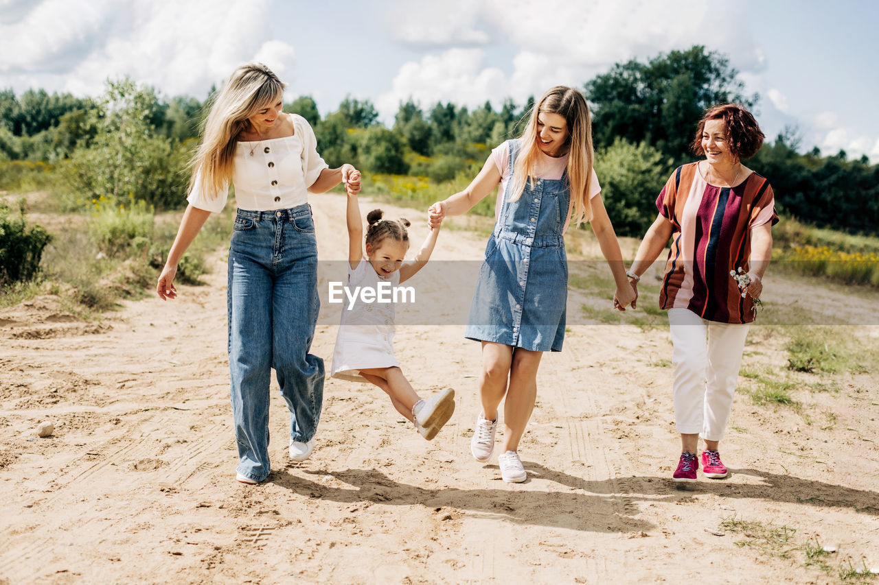 Several generations of women of the same family are walking along a dirt road outside the city