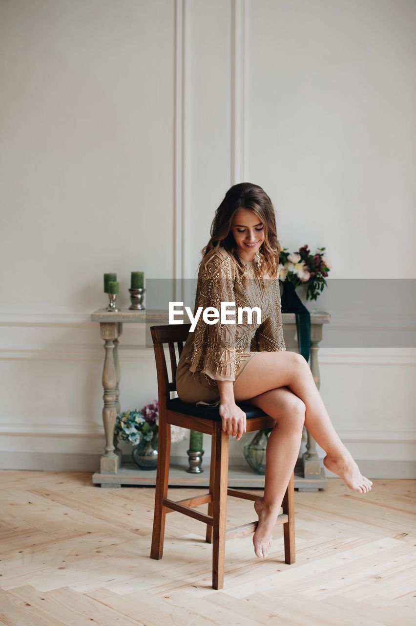 Full length of smiling young woman sitting on chair at home