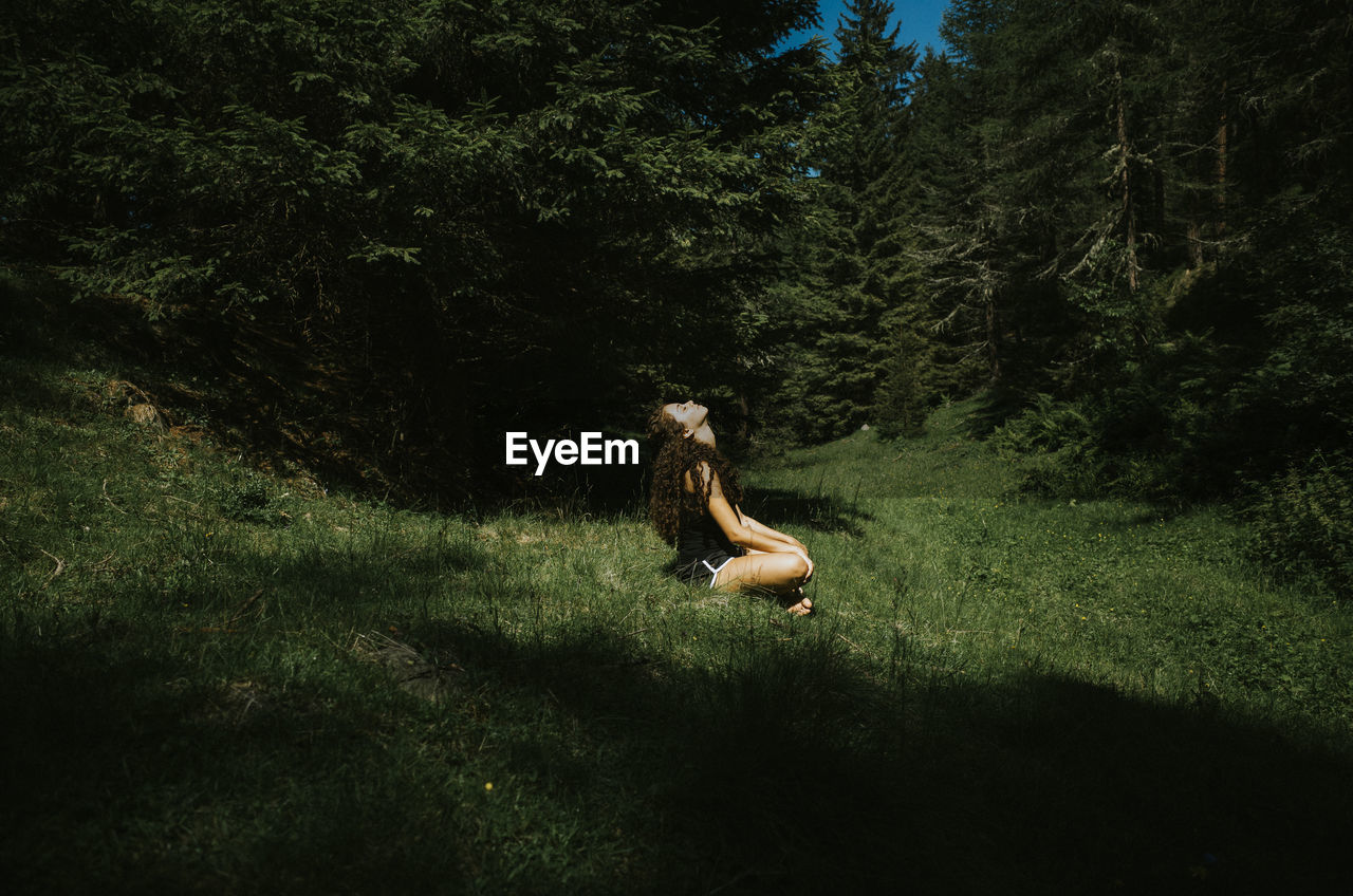 Side view of young woman sitting on grassy field during sunny day