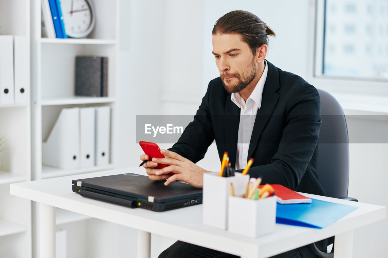 YOUNG MAN USING MOBILE PHONE WHILE SITTING IN TABLE