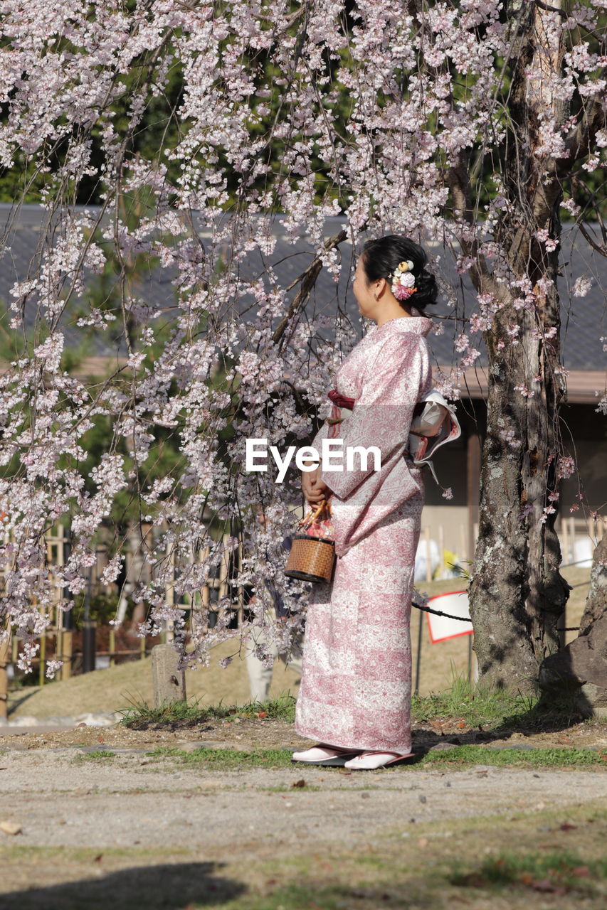 WOMAN STANDING BY TREE IN PARK