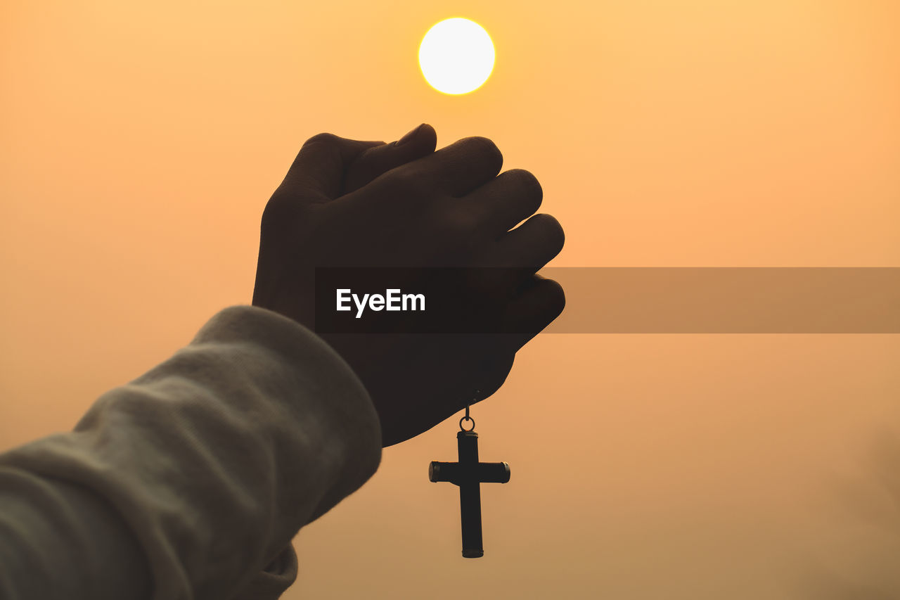 Both hands grasped the cross to pray to god. while the sun is setting or rising.