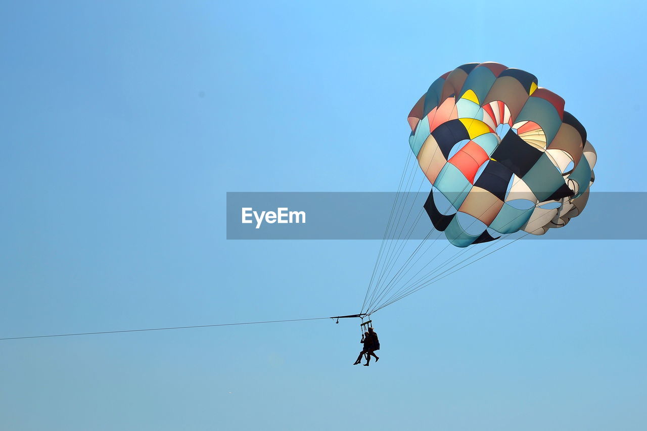 Low angle view of people paragliding against clear blue sky