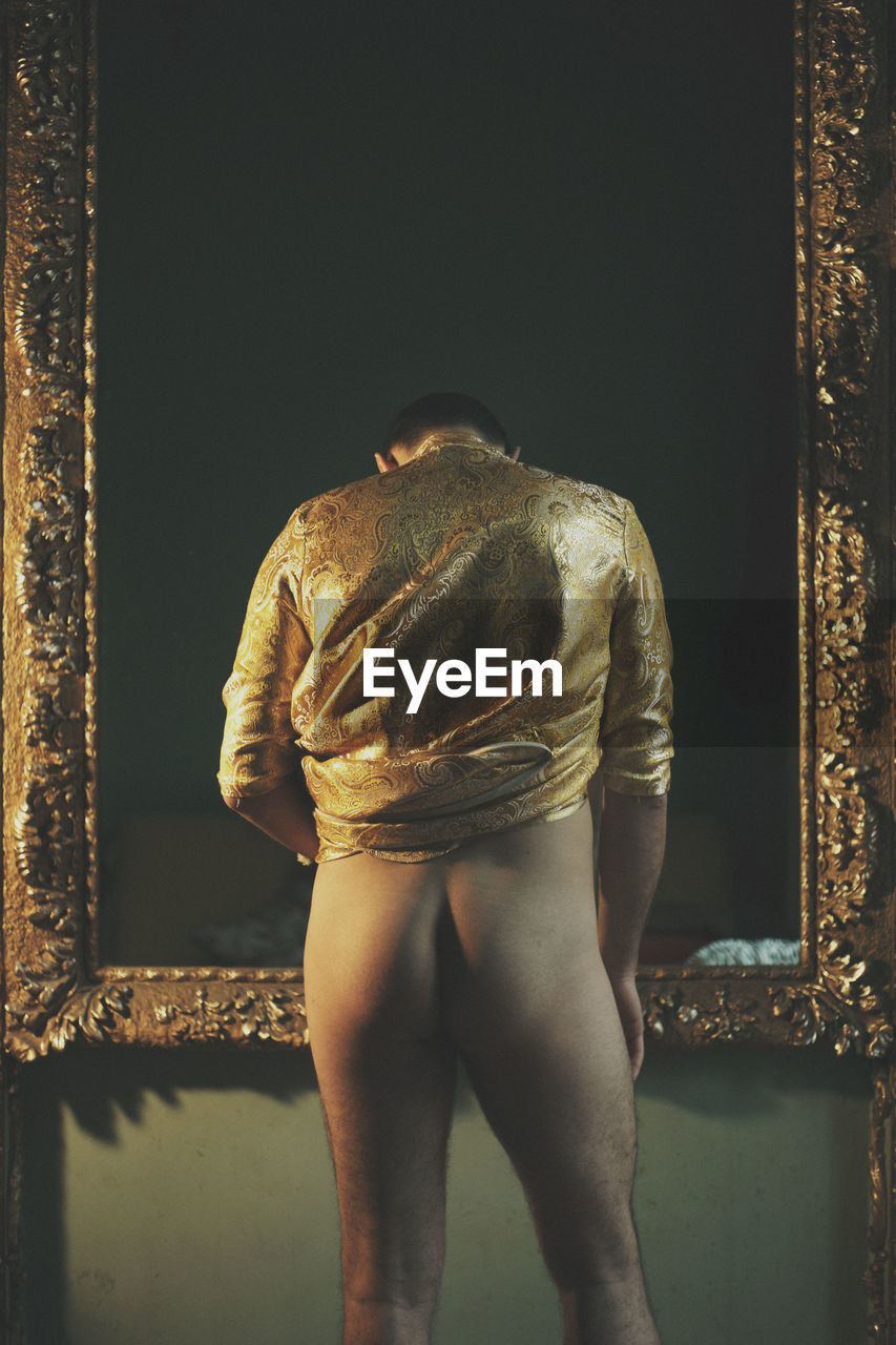 Rear view of pant less man standing against picture frame