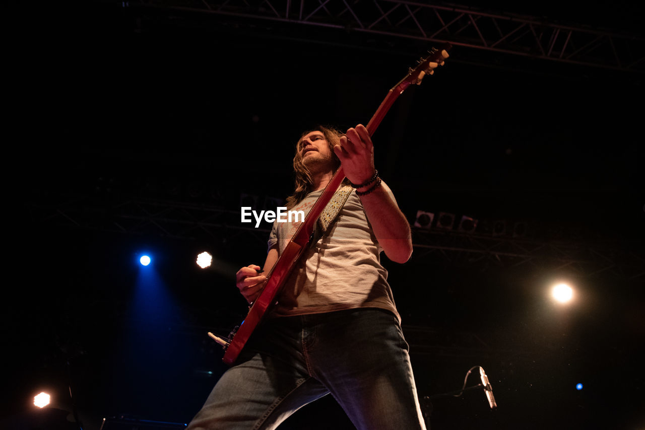 LOW ANGLE VIEW OF MAN PERFORMING AT MUSIC CONCERT