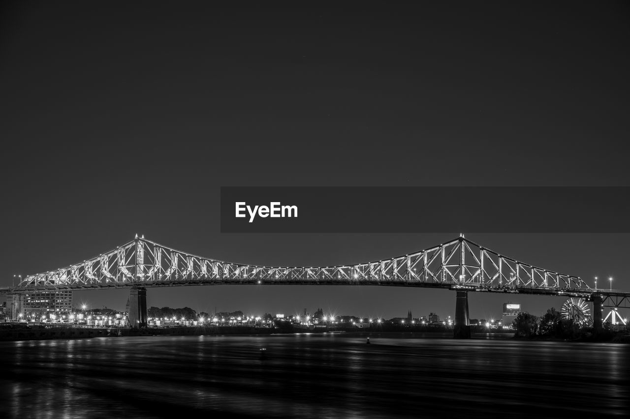 ILLUMINATED BRIDGE OVER RIVER AGAINST SKY