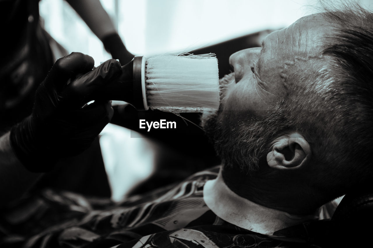 Barber applying shaving cream on face of man at salon