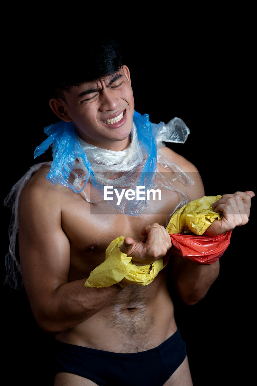 Shirtless young man holding plastic against black background