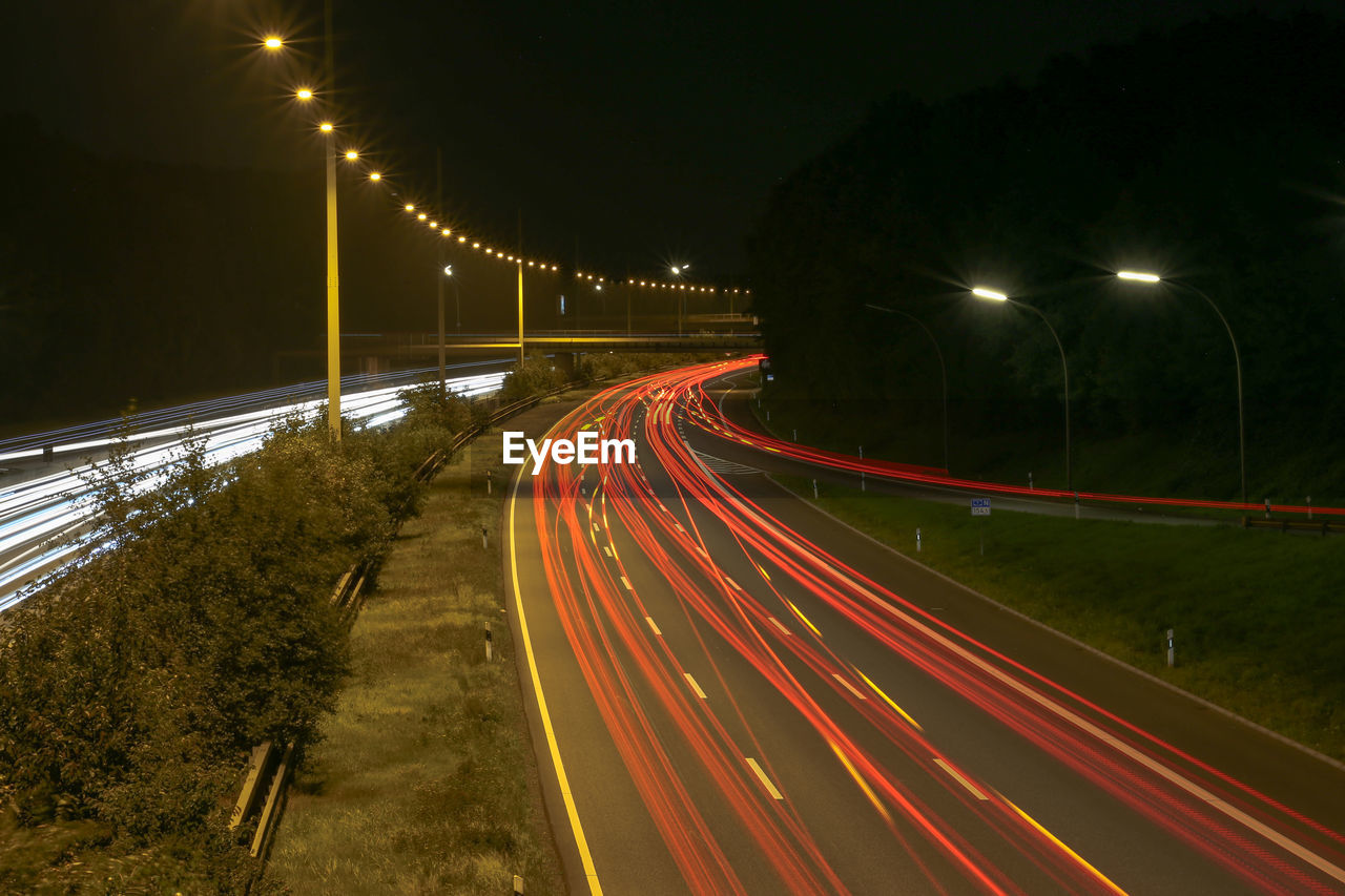 LIGHT TRAILS ON ROAD BY STREET LIGHTS AT NIGHT