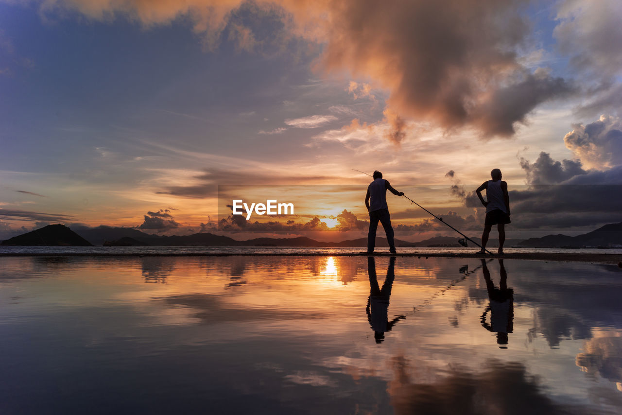 Rear view of man standing on lakeshore against sky during sunset