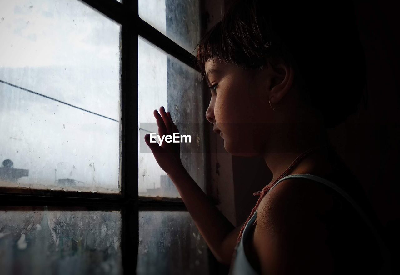 Side view of girl looking through window