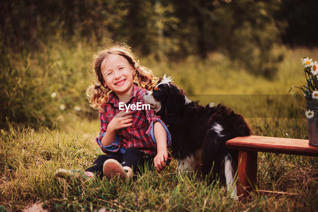 Portrait of happy girl playing with dog while sitting on field